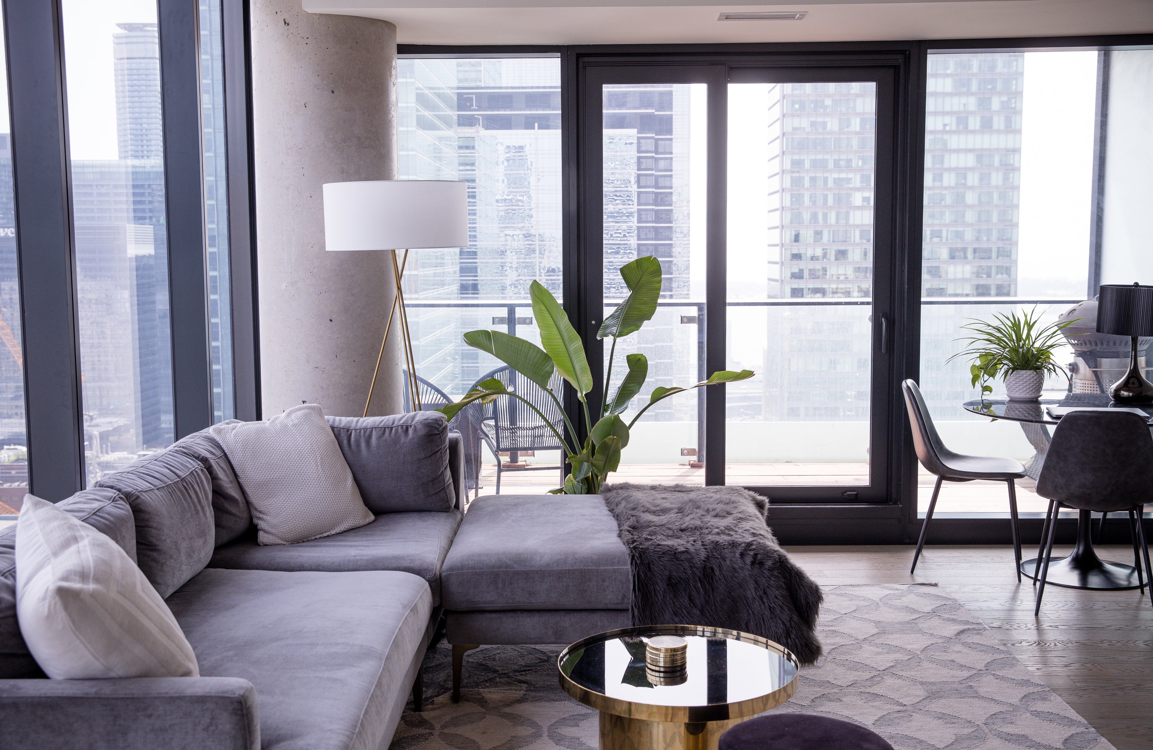 A modern apartment with large corner windows separated by a column, featuring elegant furniture including a stylish sofa, coffee table, and lamp, creating a cozy and sophisticated living space.