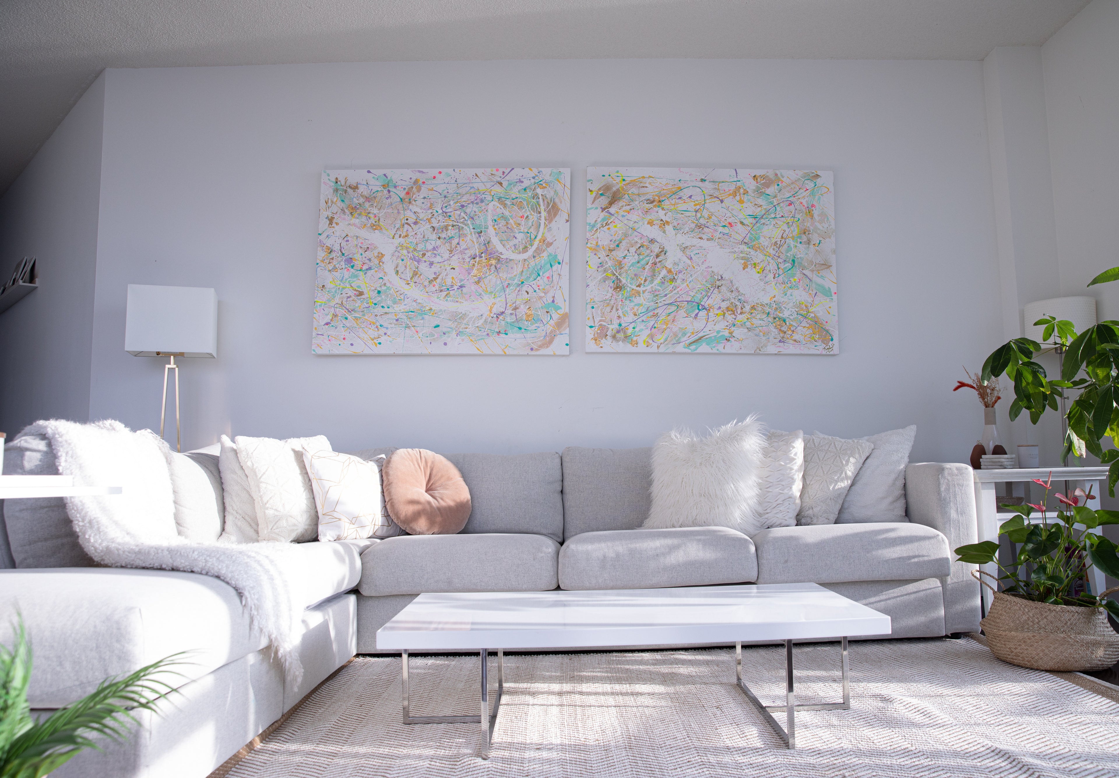A tidy living room featuring a large sofa adorned with multiple pillows, with two matching paintings symmetrically placed in the center of the wall above the sofa, creating a balanced and cozy atmosphere.
